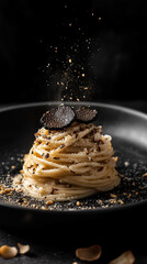 A plate of creamy pasta topped with fresh black truffle shavings and grated cheese is beautifully presented on a dark background.