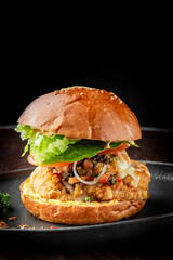 A delicious fried chicken burger topped with fresh lettuce, tomato, and mayonnaise, served on a golden sesame seed bun, presented on a black plate with parsley garnish.