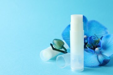 Lip balm and orchid flowers on light blue background, closeup. Space for text