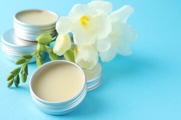 Lip balms and freesia flowers on light blue background, closeup. Space for text