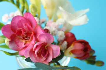 Bouquet of beautiful flowers in glass vase on light blue background, closeup