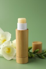 Lip balm and freesia flowers on light green background, closeup