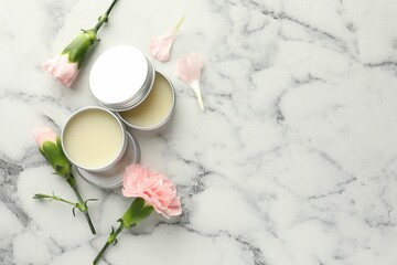 Moisturizing lip balms and pink flowers on white marble table, flat lay. Space for text