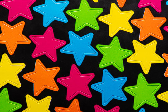 A vibrant assortment of multicolored star shapes in pink, blue, green, yellow, and orange, scattered on a black background