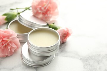 Moisturizing lip balms and pink flowers on white marble table, closeup. Space for text