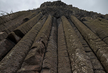 A cliff wall at Giant's Causeway, Ireland, featuring tall basalt columns under an overcast sky,...