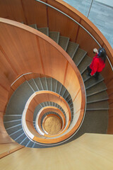 Blurred woman in a red coat walks up a spiral staircase.