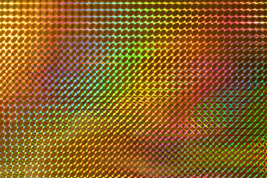 A vibrant, multicolored holographic surface featuring a pattern of raised diamond shapes, reflecting light and creating a dynamic visual effect.