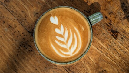 Delicious golden flat white coffee with latte art in a rustic cup on a wooden grain table
