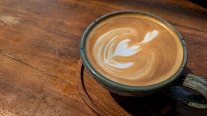 A delicious golden flat white coffee with latte art in cup on wooden coaster on wooden table