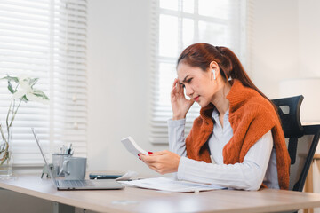 Obraz premium Cheerful Asian businesswoman celebrating success while looking at her smartphone, sitting at desk with laptop and glasses.