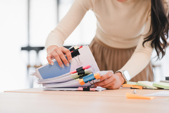 Asian businesswoman organizing documents with colorful clips on wooden desk in bright office.