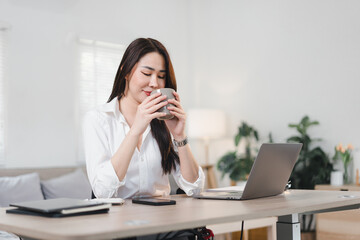 Asian businesswoman working on laptop at home, sitting on wooden table in cozy living room.