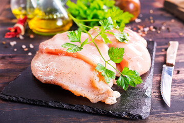 Fresh chicken breast fillet on cutting board with spices, dark rustic background.