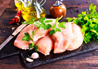Fresh chicken breast fillet on cutting board with spices, dark rustic background.