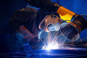 Factory industrial welder worker in workplace with spark, neon light. Professional welder fix...