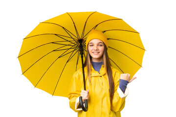 Teenager girl with rainproof coat and umbrella over isolated chroma key background pointing to the...