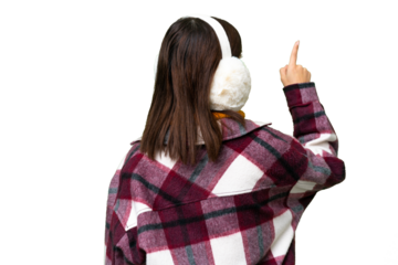 Young Russian woman wearing winter muffs over isolated chroma key background pointing back with the index finger
