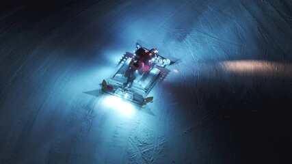 An aerial view captures a snow groomer at work on a starry night in Courchevel, France, illuminating the snowcovered landscape and majestic mountains, creating a magical winter scene