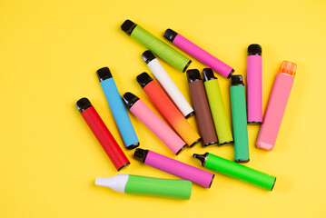 Layout of colorful disposable electronic cigarettes on a yellow background. The concept of modern smoking, vaping and nicotine. Top view