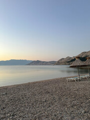 beach early morning with sun umbrella, peaceful ocean and mountains in the background