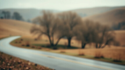 Fototapeta premium A soft, blurred background of a winding road with trees and rolling hills, creating a serene and atmospheric scene ideal for nature-themed projects.