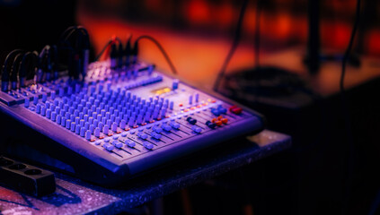 Professional audio mixing console with multiple knobs, sliders, and cables, illuminated by stage...