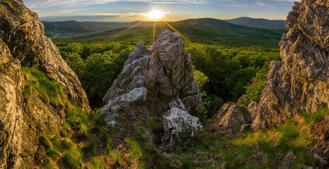 Setting sun with rays in mountain landscape with green forest and rocks. Panorama of spring landscape with forest. Walks in spring nature.