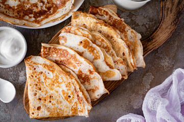 Thin large pancakes on a board on a gray background . Thin pancakes for breakfast. View from above. Close-up