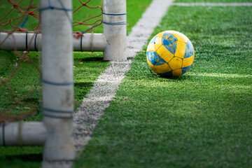 yellow football or soccer ball lying on the artificial grass with little sun ray coming through of it.