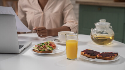 Young african american woman in the morning in the kitchen at home enjoying healthy breakfast, sitting at table working on laptop.
