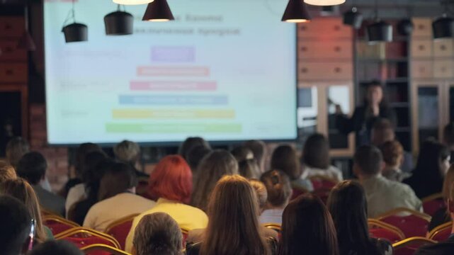 Attendees seated in auditorium listening to speaker presentation. Focus on audience participation in professional atmosphere. Ideal image for business seminar promotional materials.