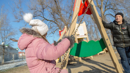 Grandfather playing with his granddaughter on the playground in the park in winter