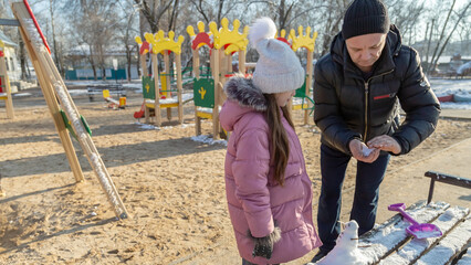 Grandfather with granddaughters making a little snowman in sunny winter day