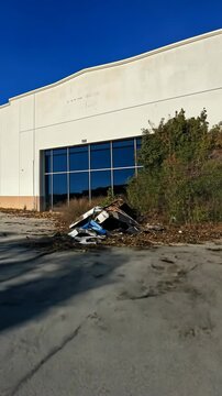Abandoned building with scattered debris and overgrown plants in a deserted location during midday
