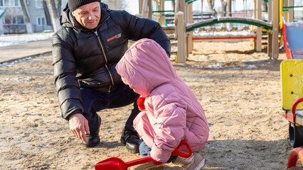 Grandfather playing with his granddaughter on the playground in the park in winter
