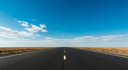 Naklejka premium Endless asphalt road stretching towards horizon under expansive blue sky