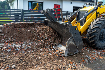 A backhoe loader carries and levels rubble on a dirt road.