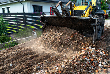 Fototapeta premium A backhoe loader carries and levels rubble on a dirt road.