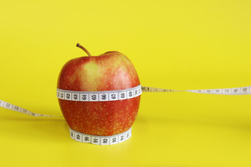Measuring tape and red ripe apple on yellow background with copy space for text. Healthy eating and weight loss concept. Composition with white measuring tape and apple. Diet. Healthy lifestyle