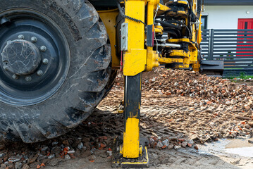 Fototapeta premium A backhoe loader raised on hydraulic cylinders lifts rubble with a telescopic bucket.