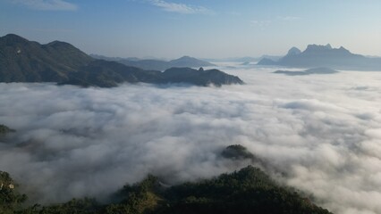 view of towering mountains enveloped in a sea of mist, with the soft glow of the morning sun casting a warm and peaceful light across the landscape. The mist creates an ethereal atmosphere, enhancing 