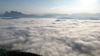 view of towering mountains enveloped in a sea of mist, with the soft glow of the morning sun casting a warm and peaceful light across the landscape. The mist creates an ethereal atmosphere, enhancing 