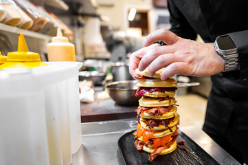 A chef meticulously stacks a towering pile of pancakes layered with various meats and toppings in a...