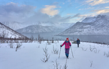 couple hiking in winter up to the Segla summit above the village of Fjordgard  at Oeyford on Senja Island in northern Norway
