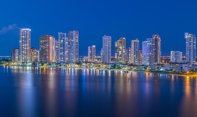 Obraz premium Coastal city skyline at dusk, reflecting in calm water, ideal for travel or architecture projects
