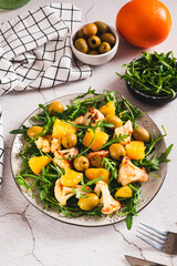 Homemade salad of cauliflower, orange, olives and greens on a plate on the table vertical view