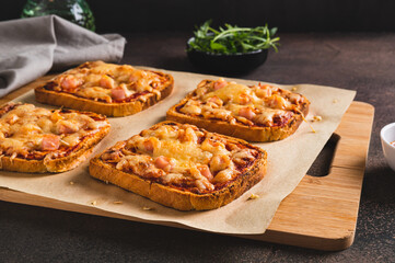 Baked sandwiches with bacon, cheese and tomato sauce on a board on a table