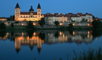 Obraz premium Lit cathedral, town reflected in calm river at dusk