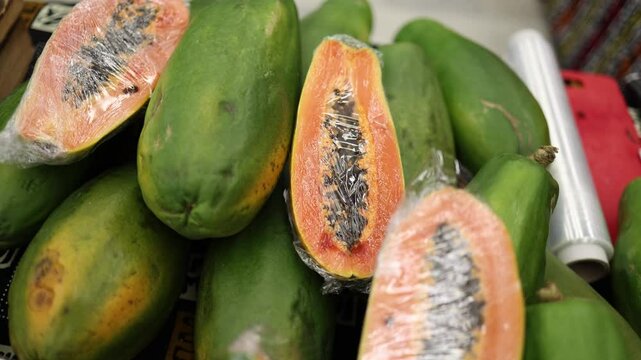 A close-up video of papayas with one sliced open, revealing the orange flesh and black seeds inside. The camera captures the green skin of the whole papayas along with the vibrant inner color.